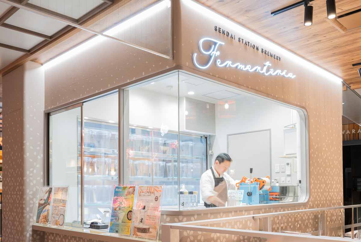 Fermenteria inside Sendai Station: an illuminated sign above a glass-fronted brewery with transparent fermentation tanks